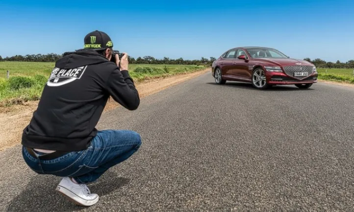 A man photographing a car on the road, capturing the moment with his camera