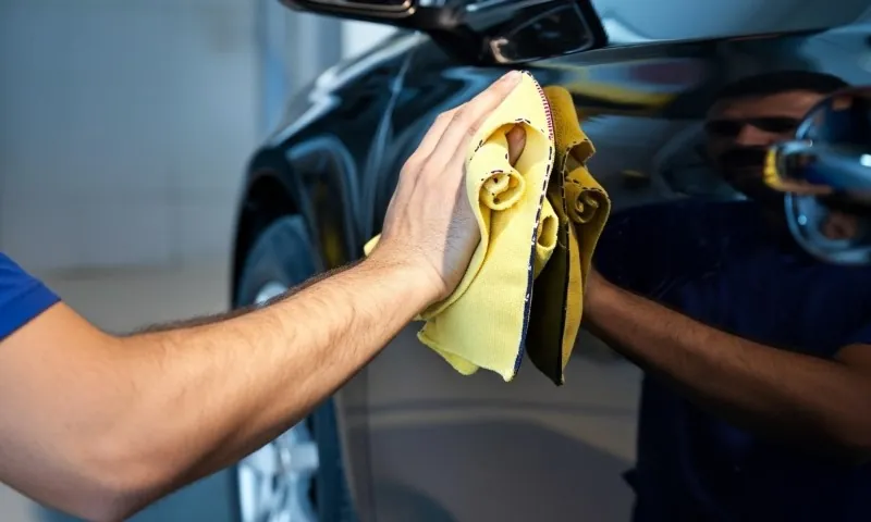 Person cleaning a car with a yellow cloth