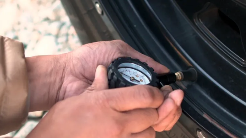 Hands use a tire gauge to check pressure as part of a routine maintenance schedule