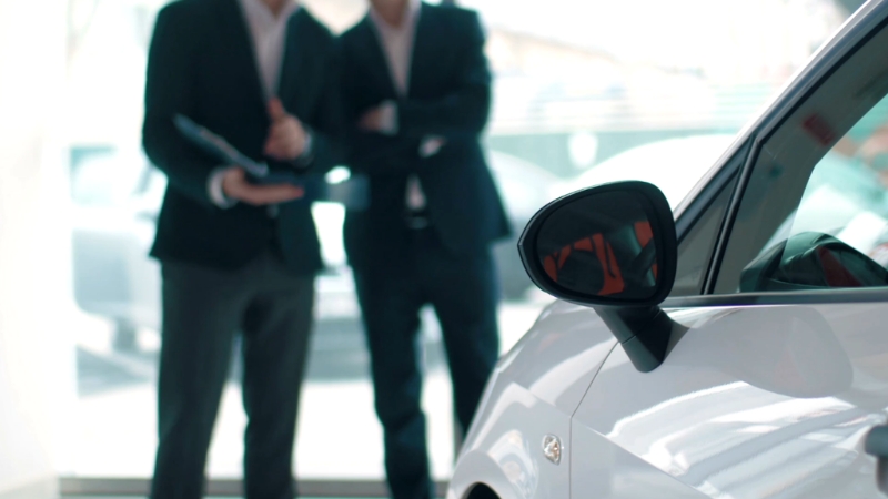 Two team members discuss operations beside a car inside a dealership showroom