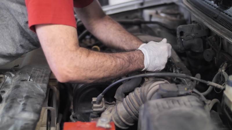 A person works under the hood with gloves on during a basic DIY car fix