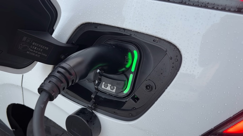 Electric vehicle charging port with DC fast charger connected, indicator lights showing active charging during outdoor use