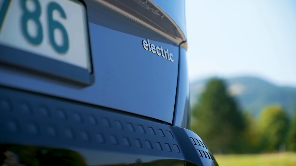 Close-up of the rear badge on an electric vehicle, showing the word “electric” on the tailgate, with a blurred outdoor background indicating everyday road use
