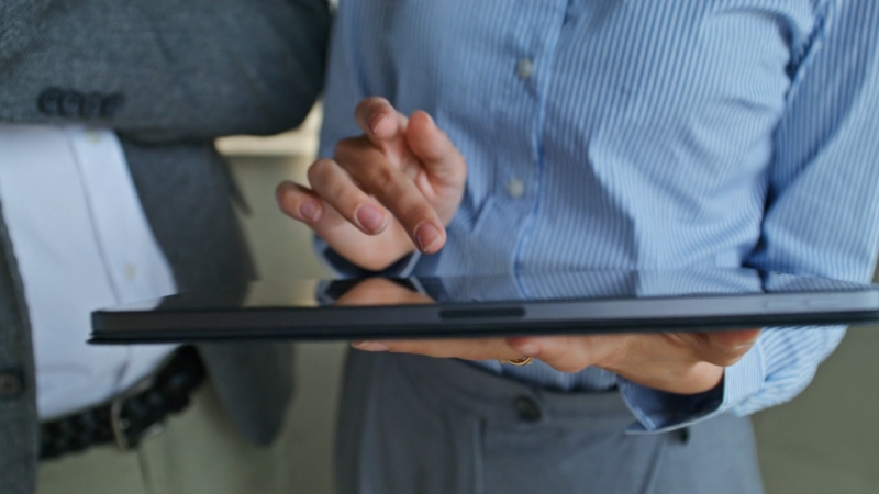 A person in business attire reviews information on a tablet during a dealership planning discussion