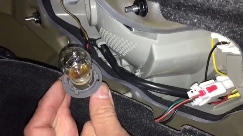 A hand removes a rear light bulb from its socket during a simple replacement
