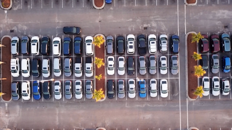 An overhead view of a large lot filled with parked cars arranged in neat rows