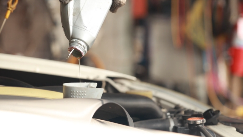 Oil pours into an engine through a small funnel during basic car maintenance tasks