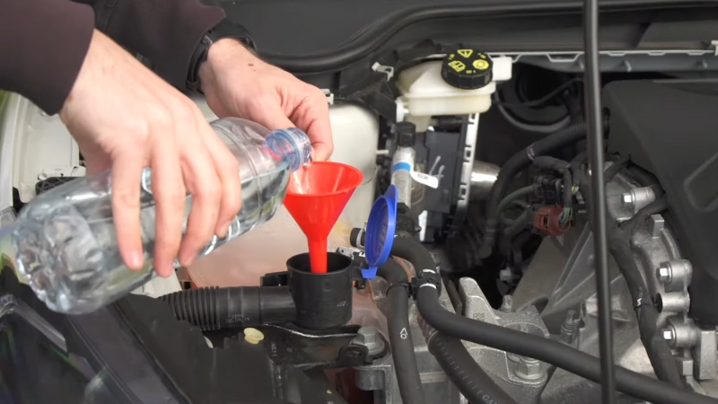 A person pours washer fluid through a funnel into the reservoir under the hood