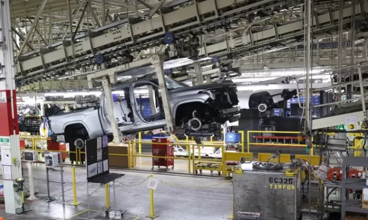 A truck is being assembled in the factory, with workers and machinery visible in the background