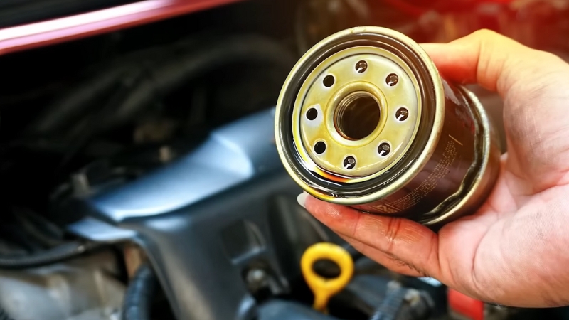 A hand holds a new oil filter above the engine bay during an oil change
