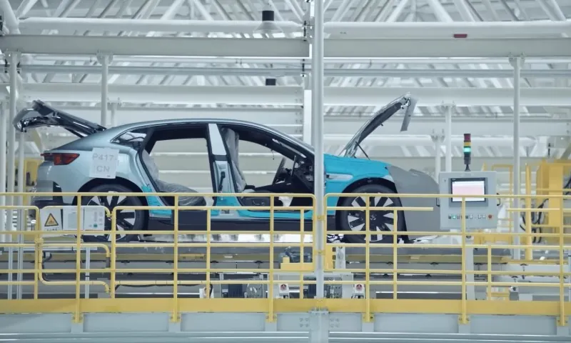 Sleek blue car on factory assembly line, doors and hood open, surrounded by yellow railings