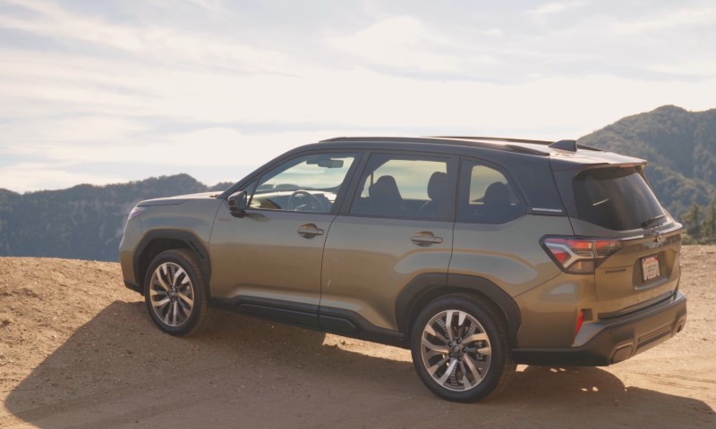 A metallic Subaru Forester parked on a sandy hill, overlooking scenic mountains under a clear sky