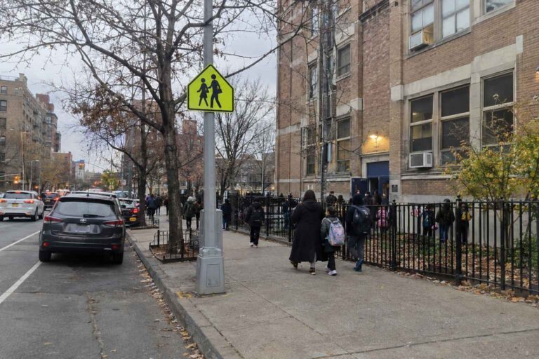 Families walk past a school crossing sign outside a New York City school.