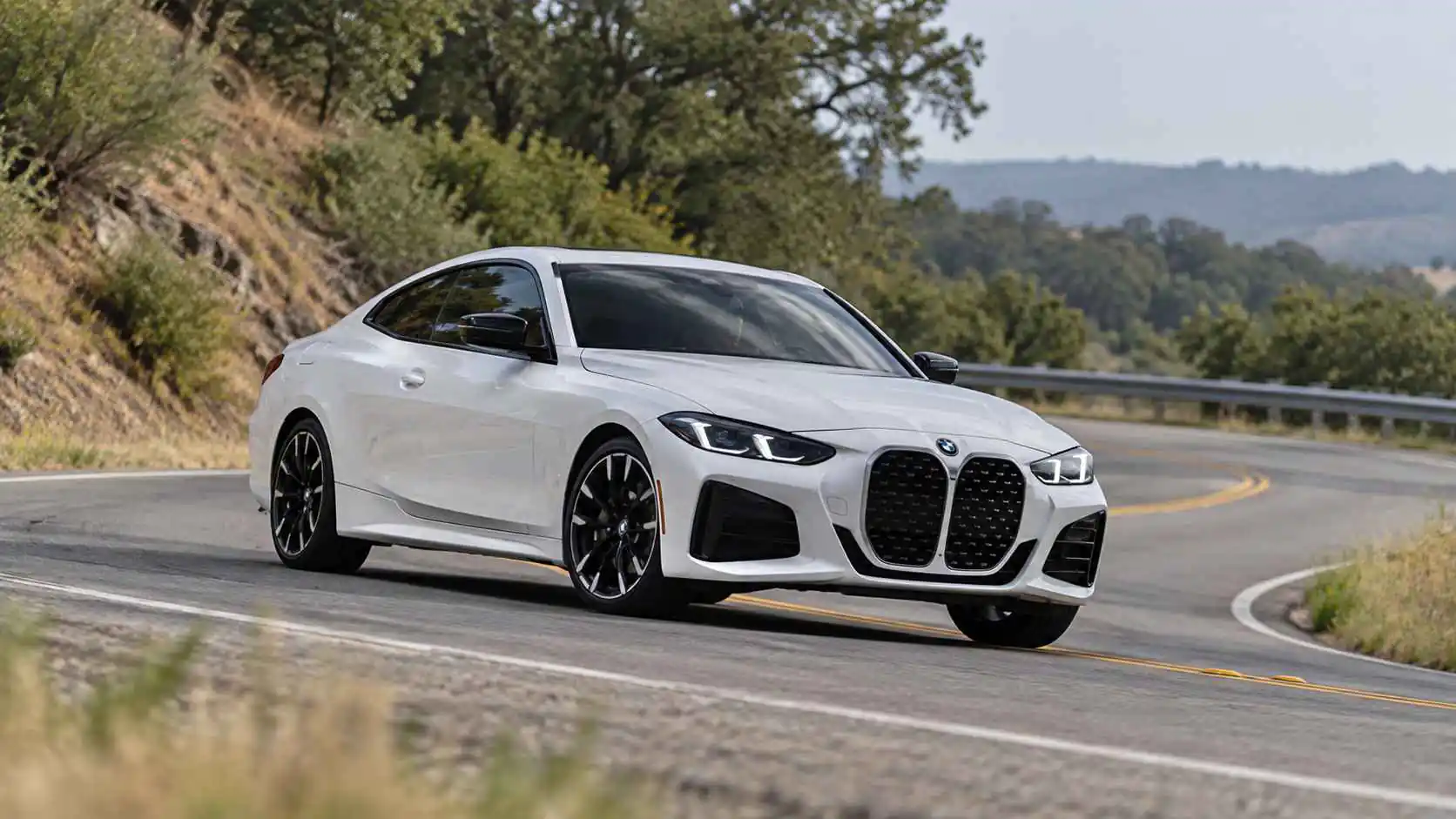 White BMW 430i driving through a bend on a country road.